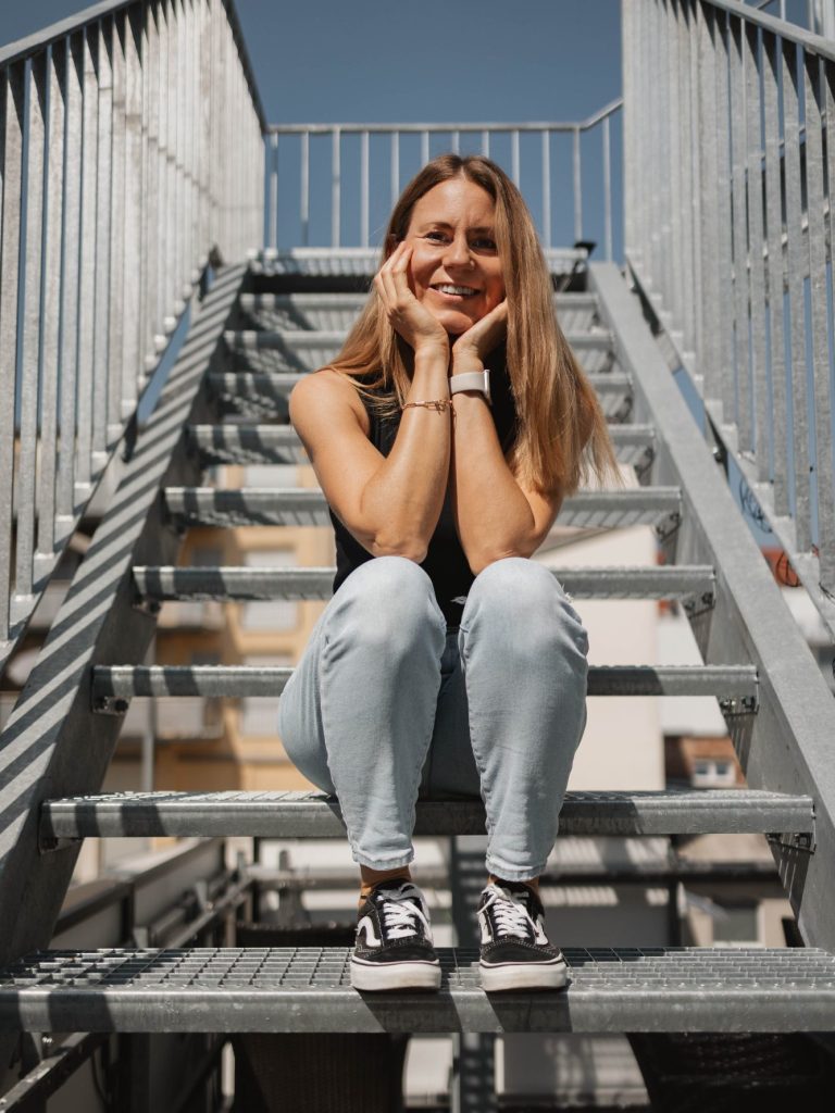 Lena Getto sitz auf untere Stufen einer Industrie-Stahltreppe im Freien.